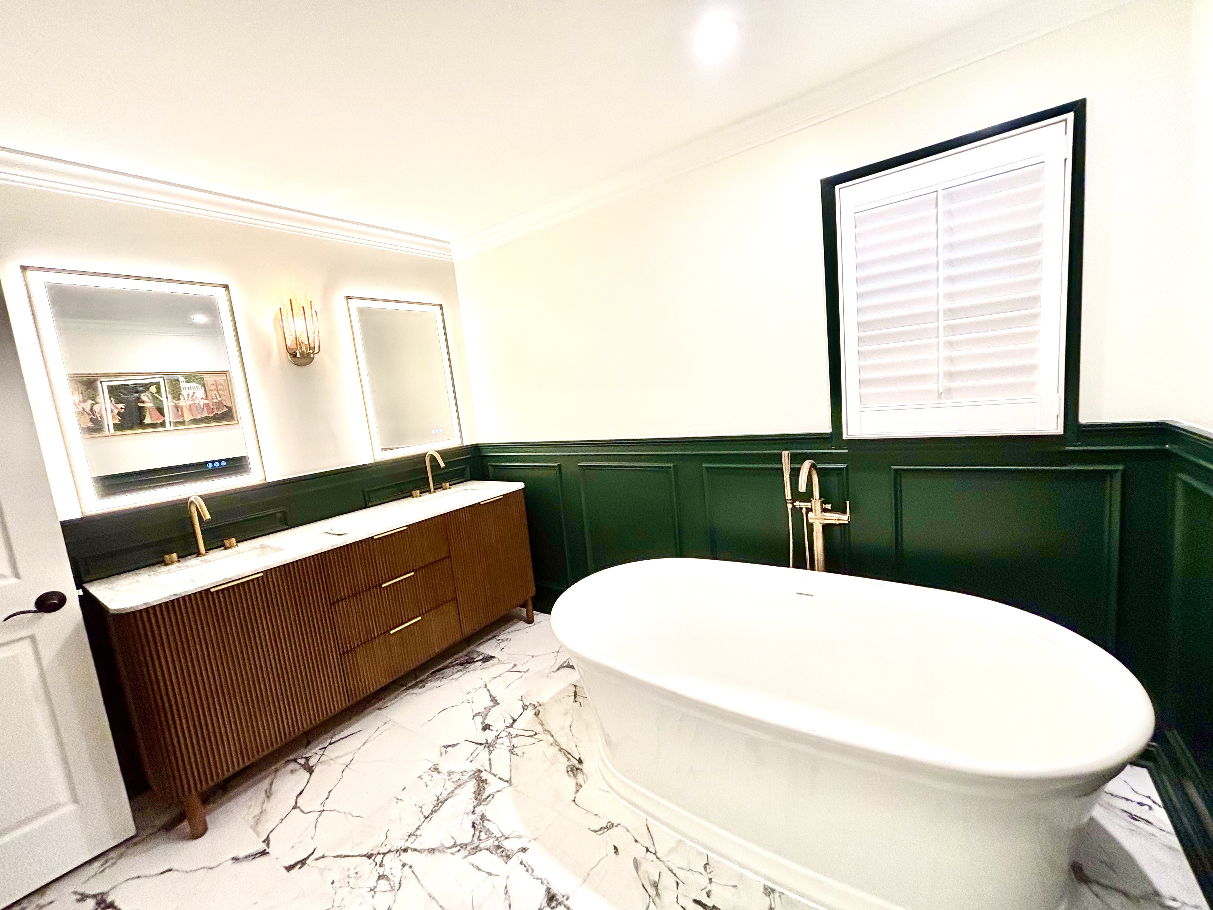 Wide view of the master bathroom: double vanity with backlit mirrors, freestanding tub and green wainscoting
