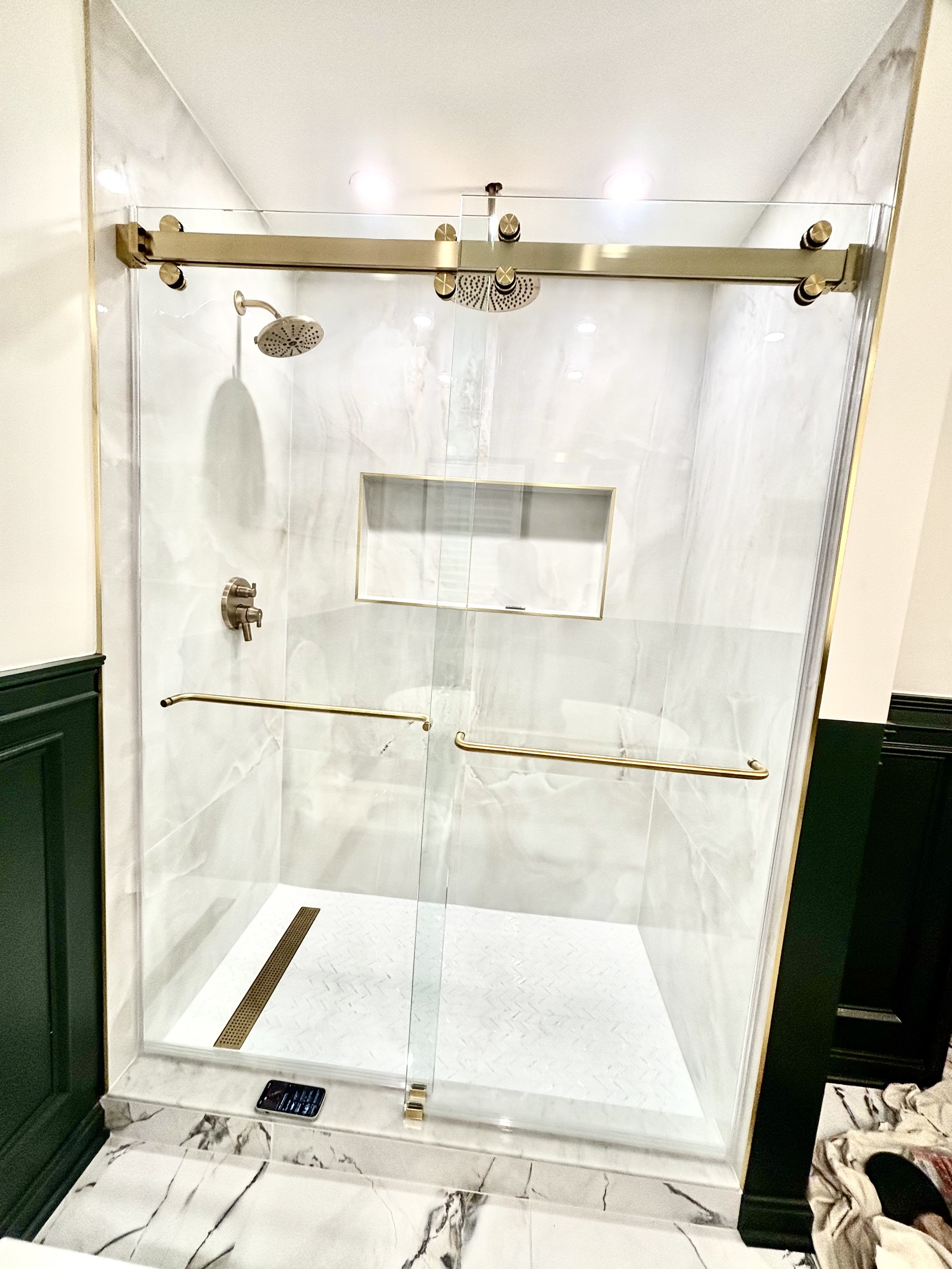 Walk-in shower with a frameless glass sliding door on a gold track and gold grab bars